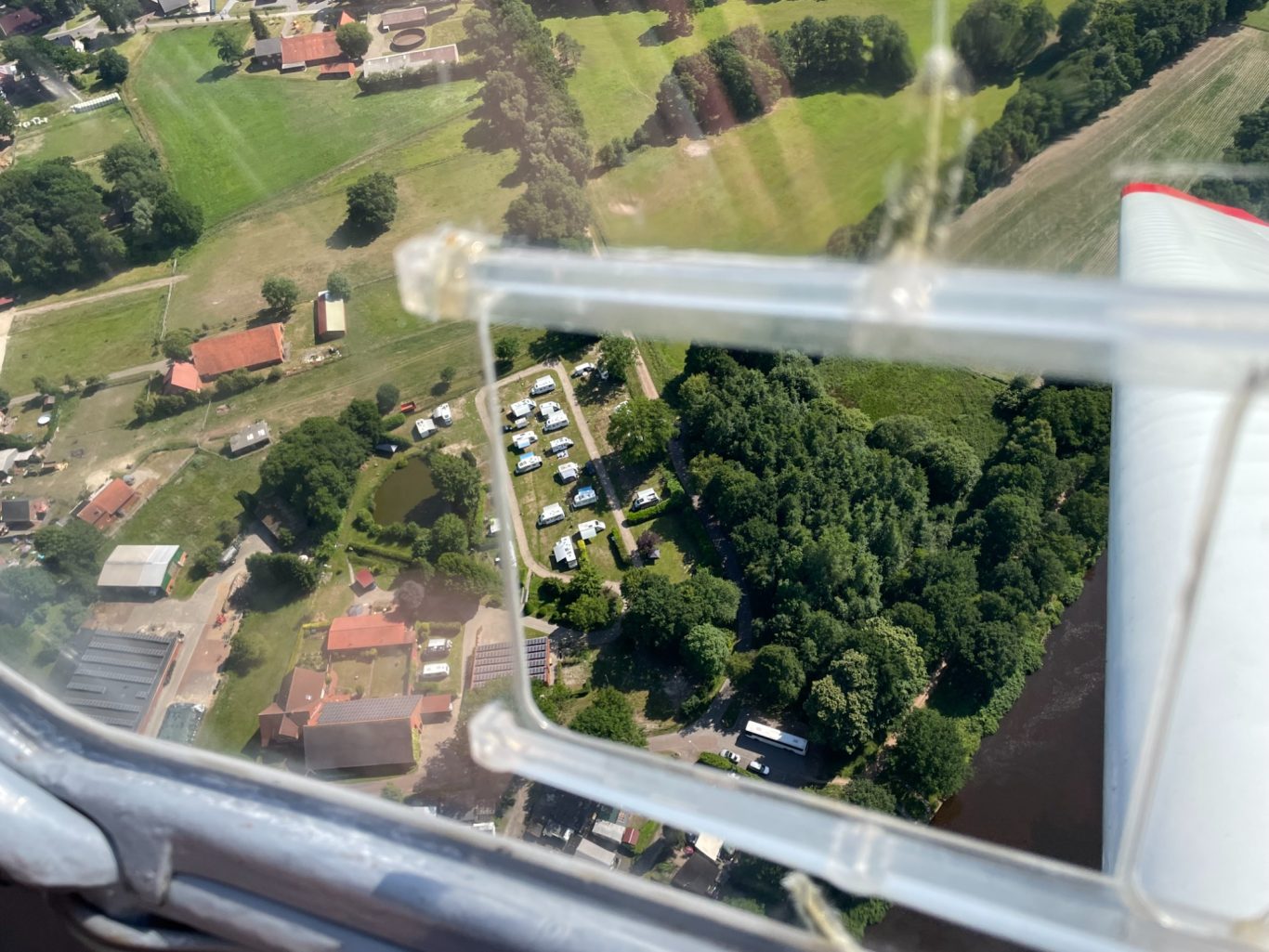 Luftaufnahme eines Campingplatzes mit Zelten, umgeben von Bäumen und Wiesen.