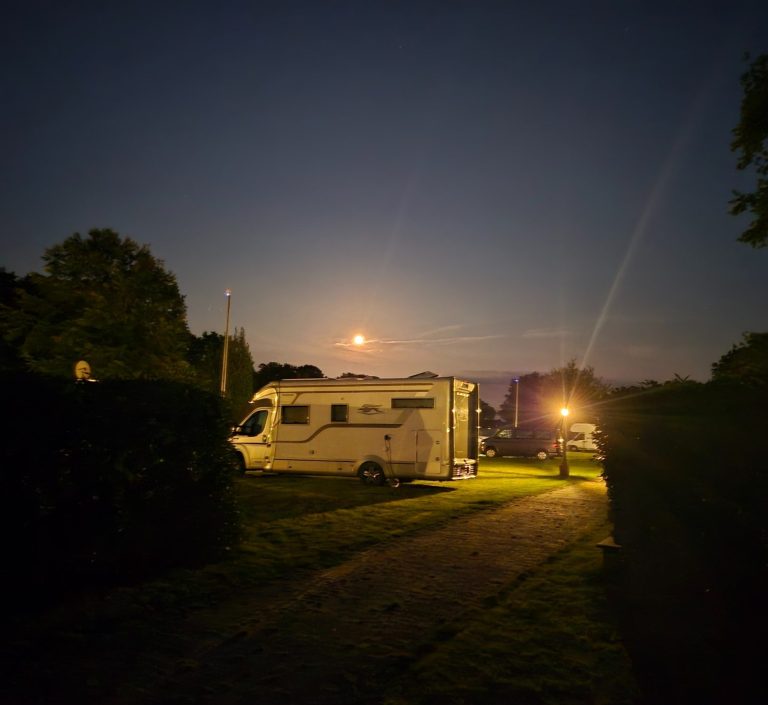 Dämmerung am Teich mit spiegelndem Wasser und sanftem Licht im Hintergrund.